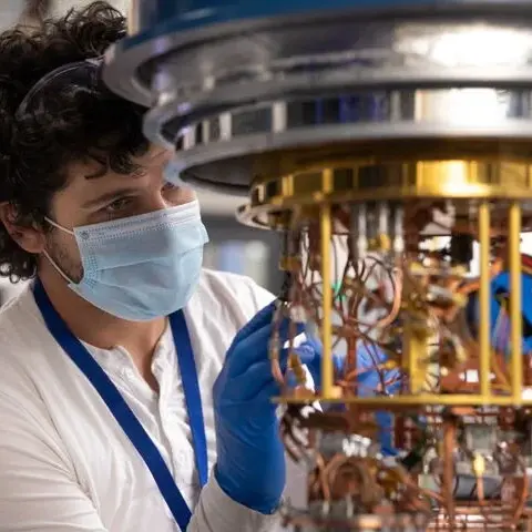 A man with a mask on working in a lab on quantum computer hardware.